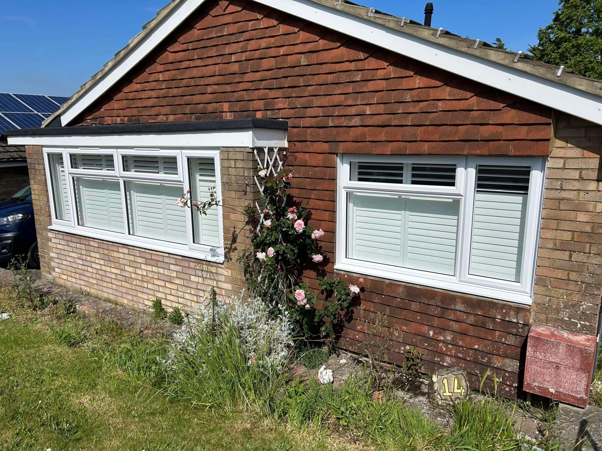 Modern window blinds installed on a brick house with garden, showcasing shading solutions.