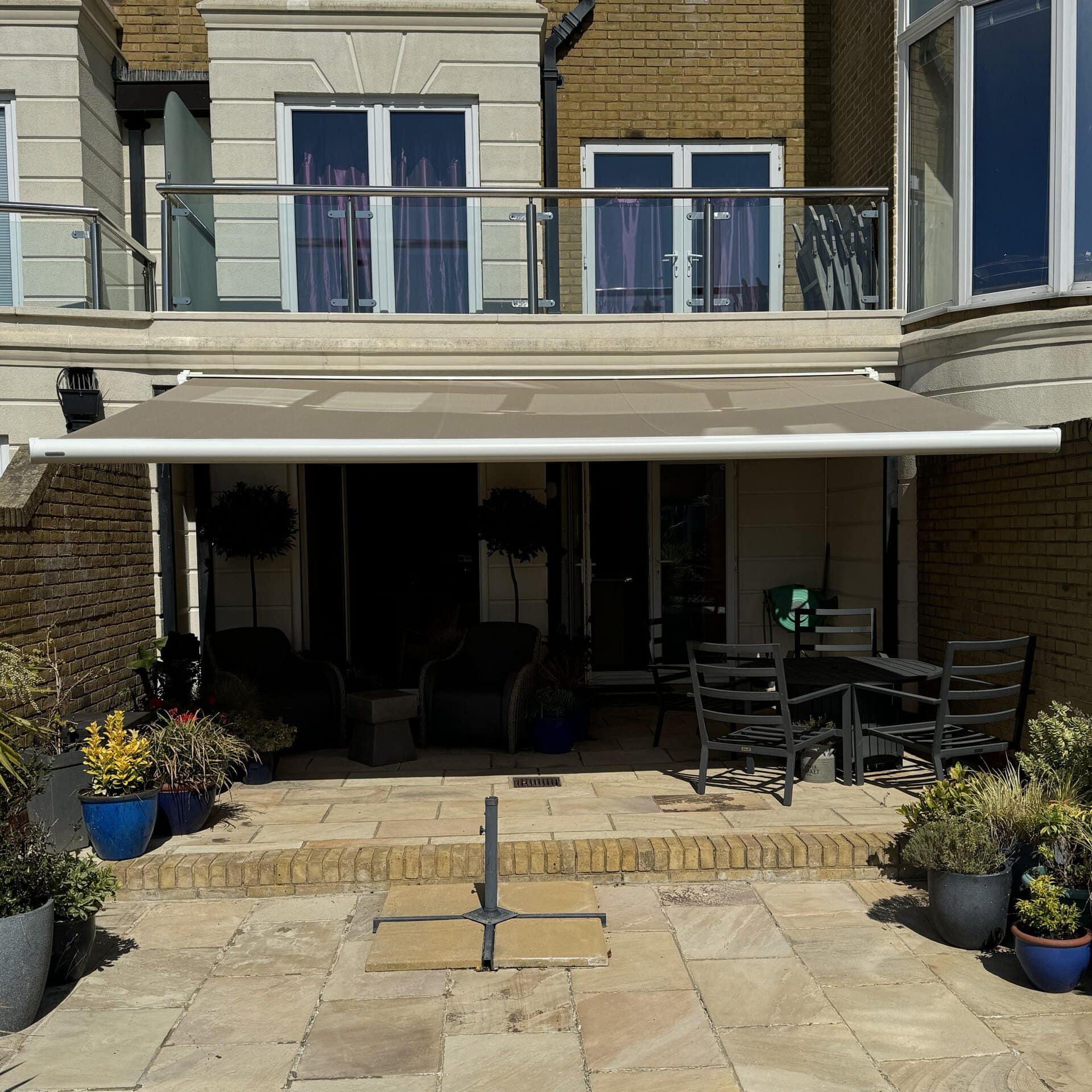 Retractable awning providing shade over a modern outdoor patio area with seating and potted plants.