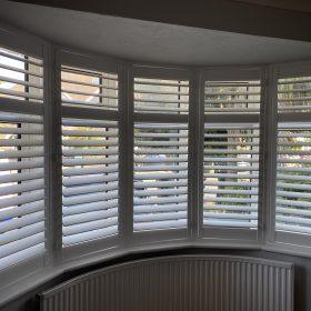 Interior view of white plantation shutters in a bay window, showcasing shading solutions.