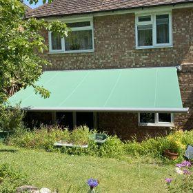 Green retractable garden awning providing outdoor shade for patio and garden area.