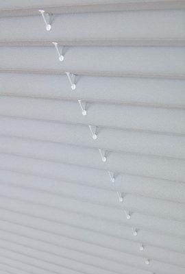 Modern white window blinds with adjustable slats for light control.
