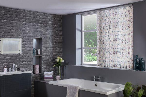Modern bathroom with patterned window curtain and grey brick wall.