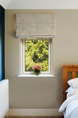 Modern window with beige Roman blind and view of greenery outside.