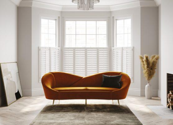 Modern living room with large bay window and white shutters, stylish interior design.