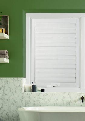 Modern white window shutter with blackout blind in a green bathroom.