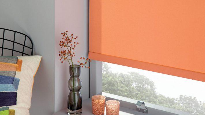 Modern orange roller blind installed in a contemporary bedroom for sun protection and privacy.