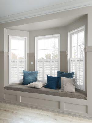 Modern window with custom white shutters and cushion seating, showcasing shading solutions.