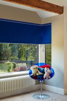 Modern blue roller blind installed in a bright room with a view of greenery.