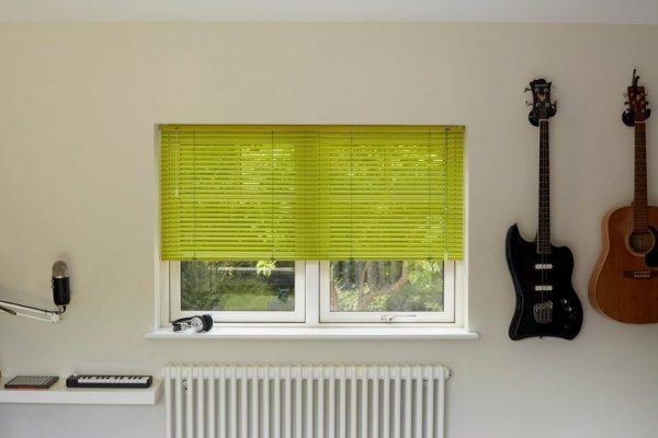 Bright green window blinds installed in a modern room with guitars on the wall.