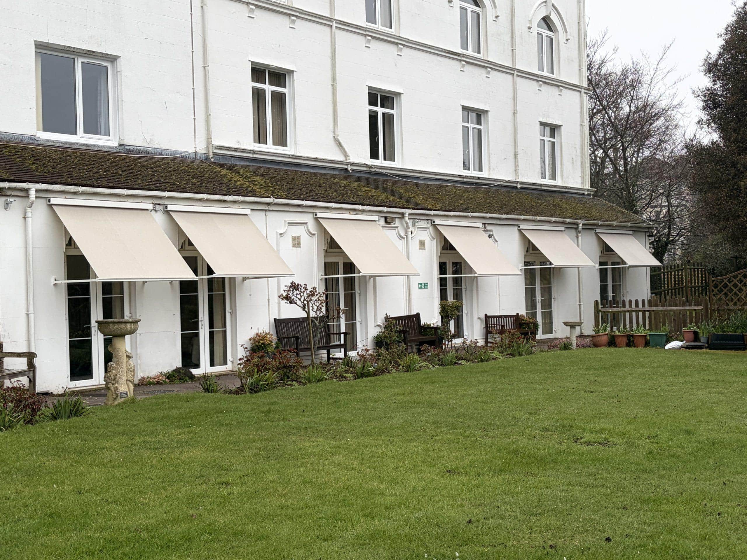 Modern shading canopies installed on a white building with garden area, enhancing outdoor comfort an.